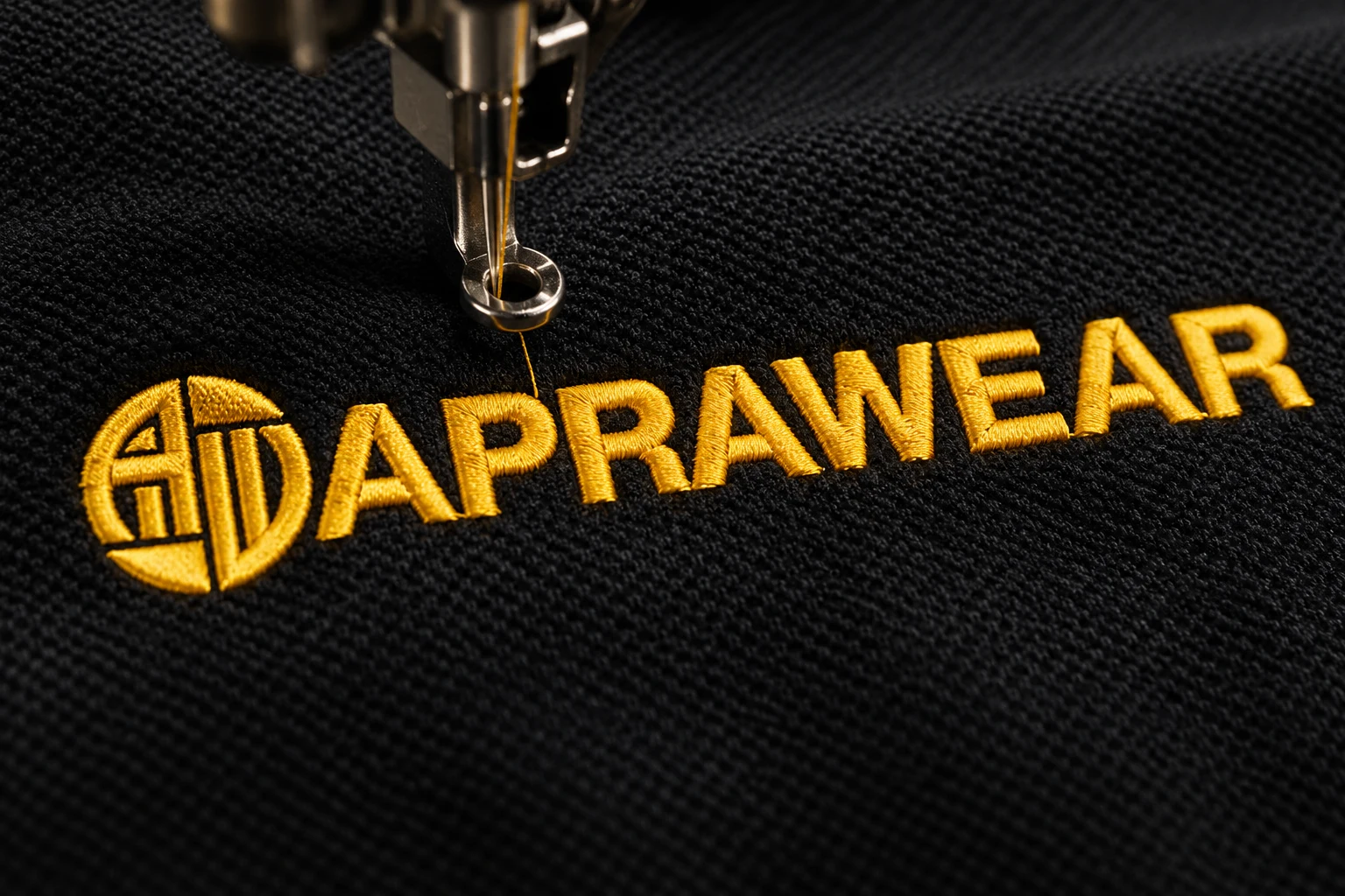 Close-up of APRAWEAR gold logo embroidery on black workwear fabric